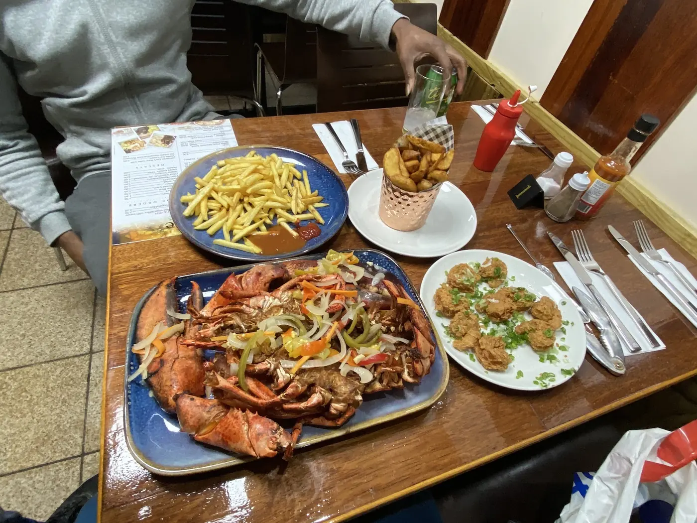 A laid table at Better Taste Cuisine with a large platter of whole lobster and grilled seafood, chips and dumplings